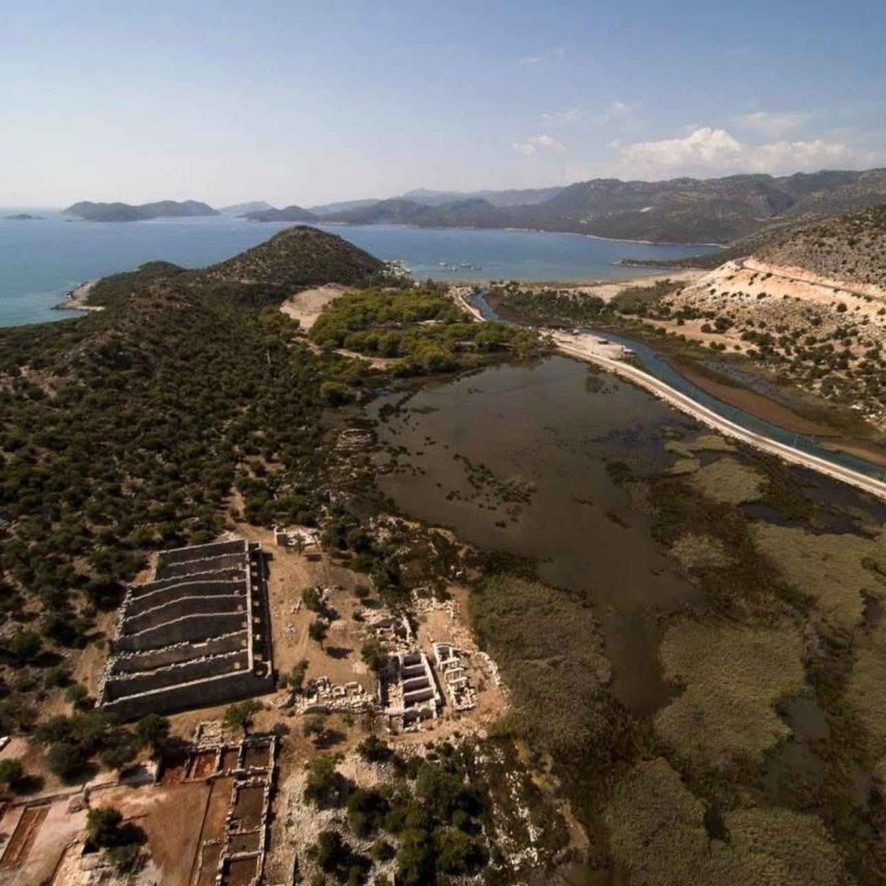 Andriake antik limanı havadan: solda Hadrian dönemi tahıl ambarının bölmeli duvarları, ortada limanın dolup bataklığa dönmüş hâli, arkada Çayağzı iskelesi ve deniz