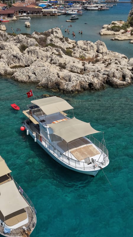 Poseidon 07 off Kaleköy from directly overhead, moored to a rocky shore in turquoise water