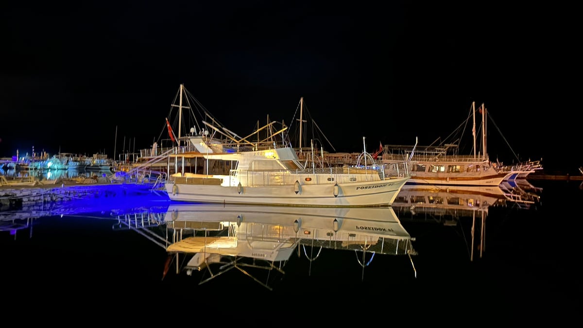 Üçağız harbour at night — Poseidon 07 and the boats beside her, reflected in the water